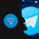 A silhouette of a hand holding a phone with the TON coin logo on it in front of a Telegram messaging app logo.